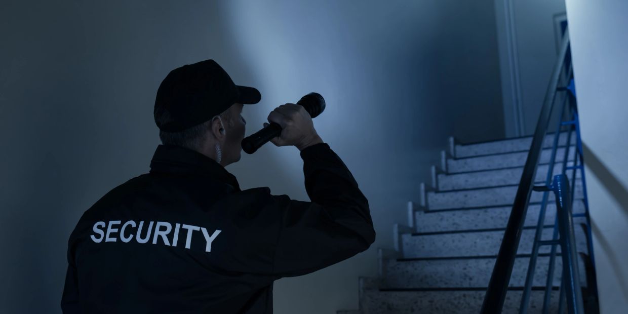 Security guard shines flashlight on stairway in dark.