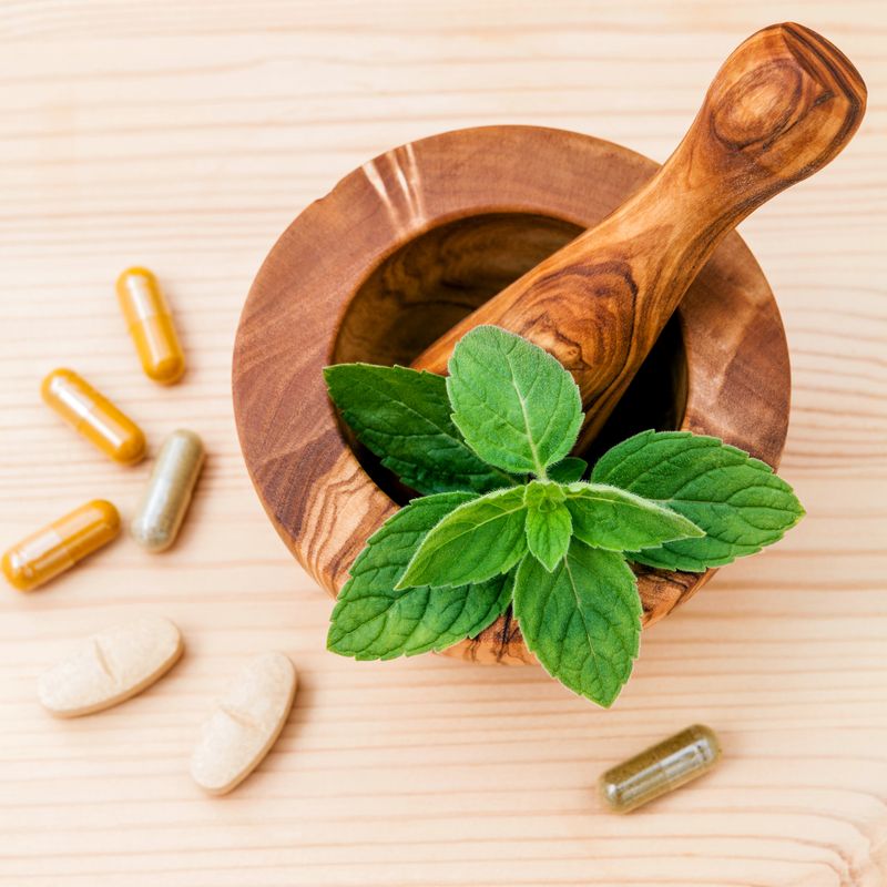 Fresh  peppermint leaves in olive wood mortar  and capsule of herbal medicine . Alternative health care concept setup on wooden background.