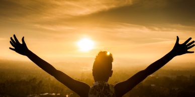 Person embracing a golden sunset with arms wide open.