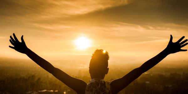 Person embracing a golden sunset with arms wide open.