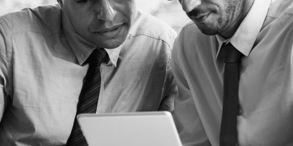 Deux hommes en chemises et cravates regardent une tablette.