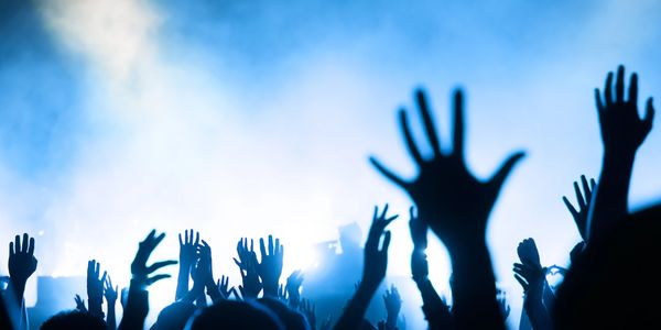 Silhouetted hands raised at a lively concert with bright blue stage lights.
