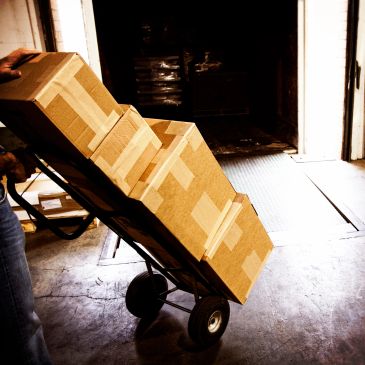 Hand truck loaded with cardboard boxes in warehouse.