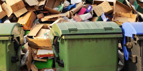 Overflowing trash bins with scattered cardboard boxes behind them.