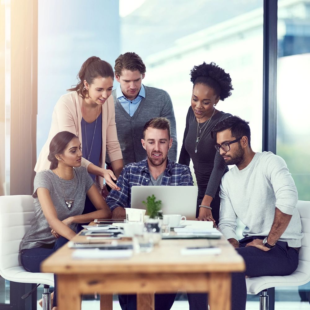 A diverse team collaborating around a laptop in a bright office.