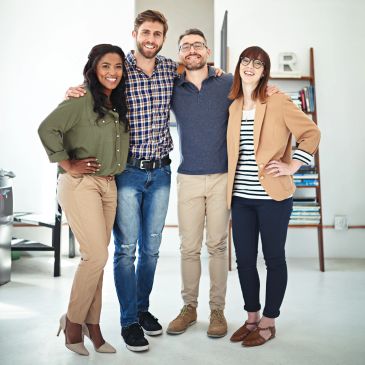 Four diverse colleagues smiling and posing together in a bright office.