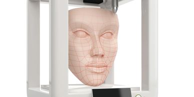 3D printer creating a detailed human face model with grid lines.