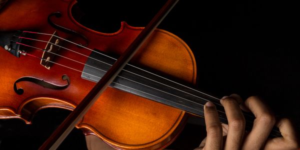 Close-up of hands playing a violin against a black background.