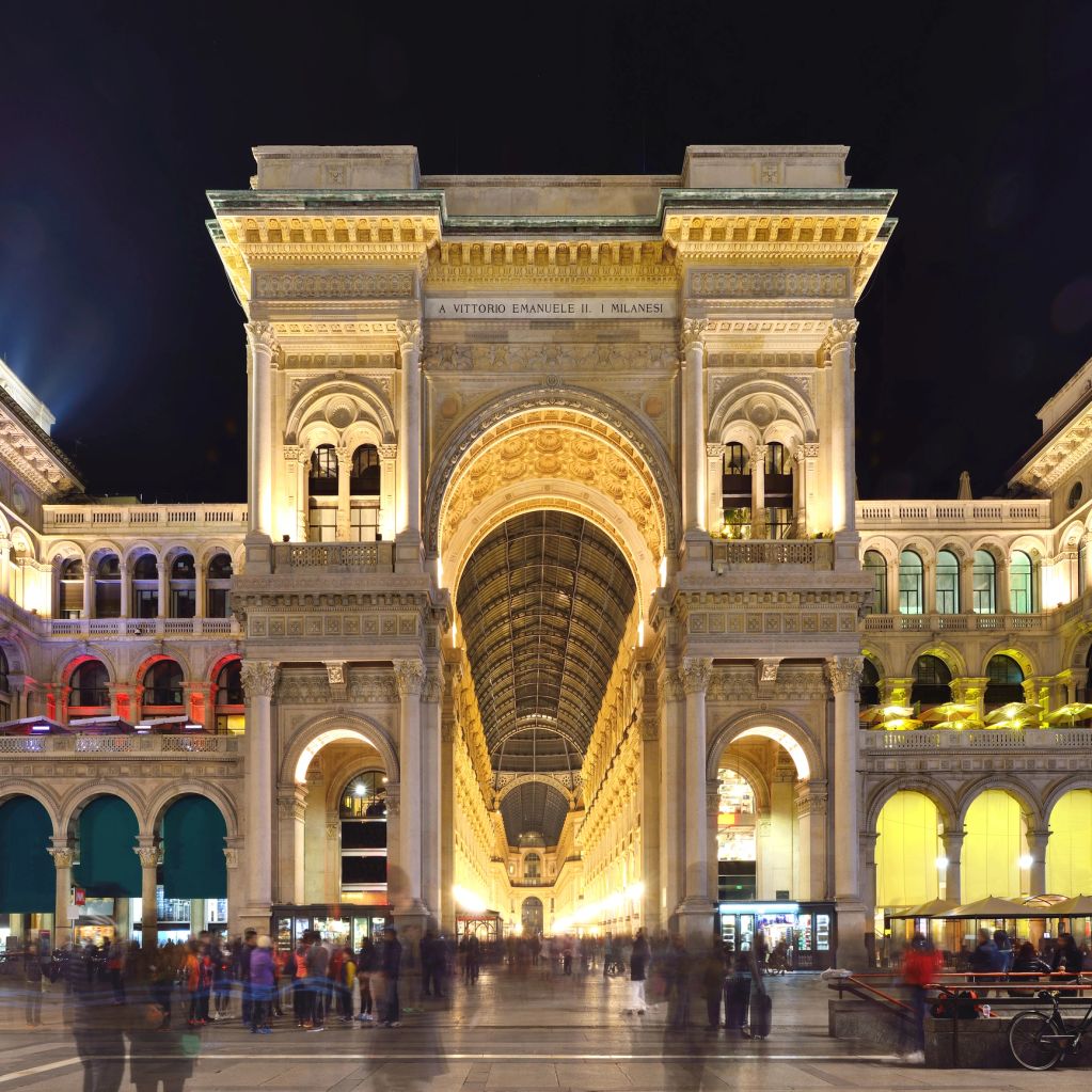 Illuminated historic archway entrance at night with people walking.