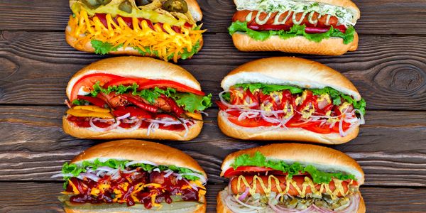 Six gourmet hot dogs with various toppings on a wooden surface.