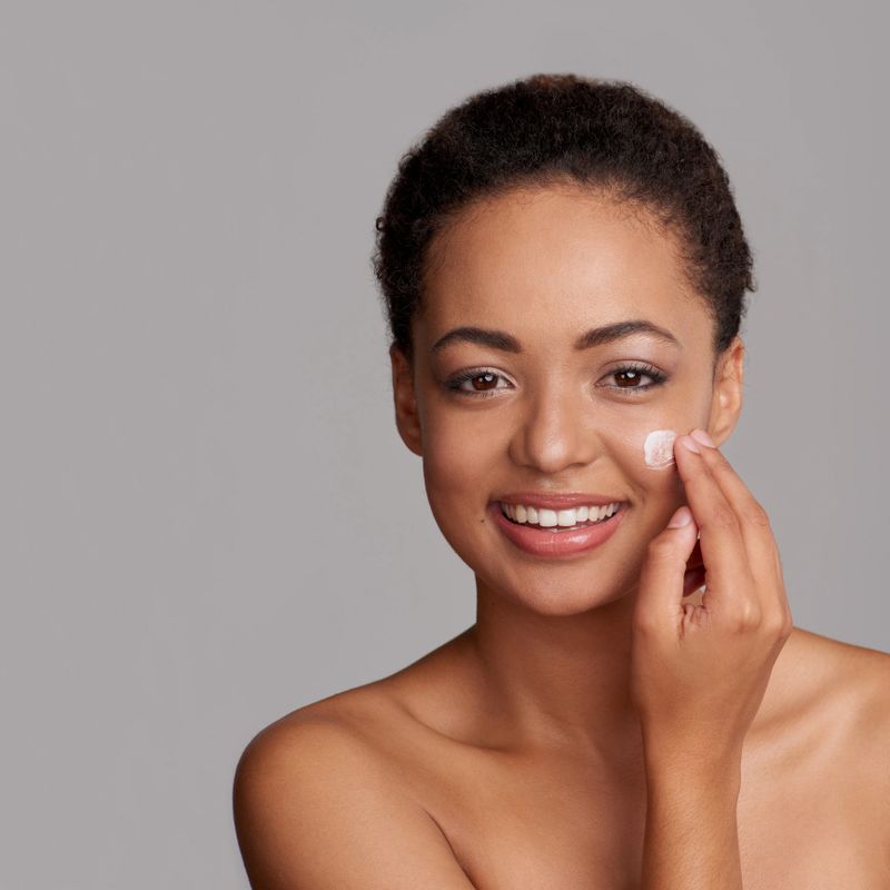Studio shot of a beautiful young woman applying moisturizer to her face