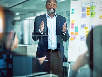 Businessman presenting ideas with sticky notes on a glass board in an office meeting.