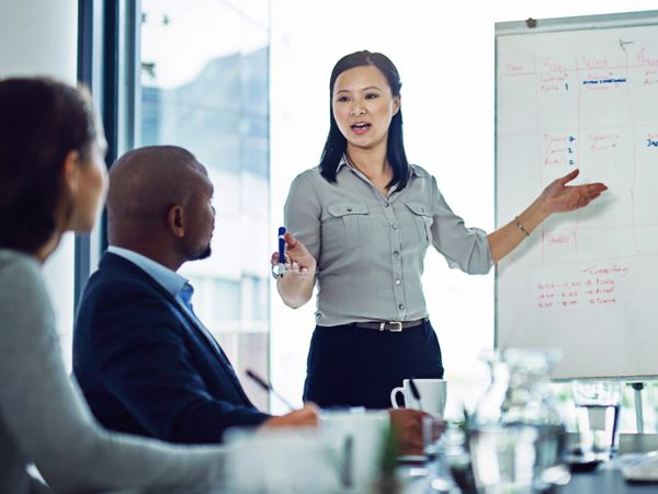 A woman leads a business meeting presenting ideas on a whiteboard.