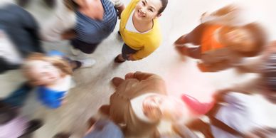 A woman in yellow stands smiling among a blurred crowd, looking up.