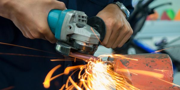 Person using a handheld grinder producing sparks while working on metal.