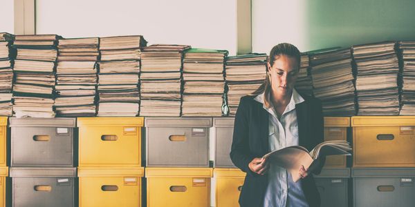 A woman reading documents in front of stacked files and yellow storage boxes.