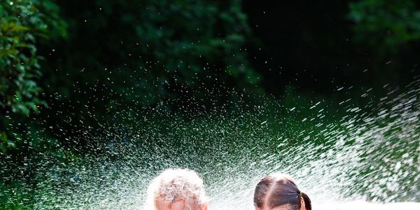 Two children playing and splashing water outdoors on a sunny day.