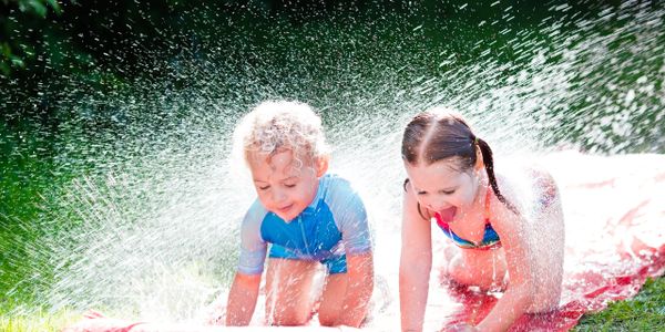 Two children playing and splashing water outdoors on a sunny day.