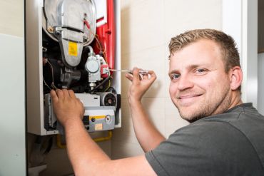 Technician repairing a boiler with a screwdriver.