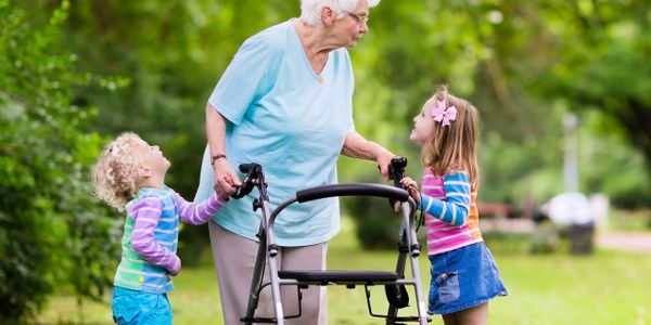 Elderly woman with walker chatting with two young children outdoors.