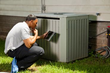 Technician inspecting air conditioning unit with tablet.