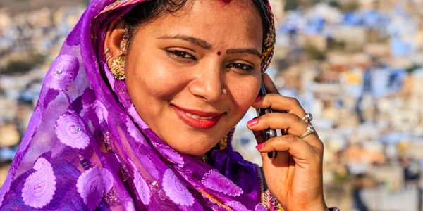 Smiling woman in a vibrant purple sari talking on a mobile phone outdoors.