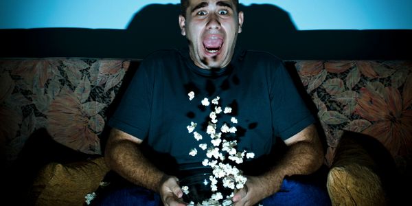 Man shocked while watching TV, popcorn flying from bowl.