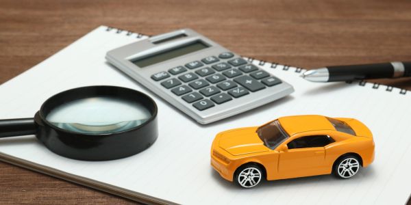 Magnifying glass, calculator, pen, and toy car on a notebook.