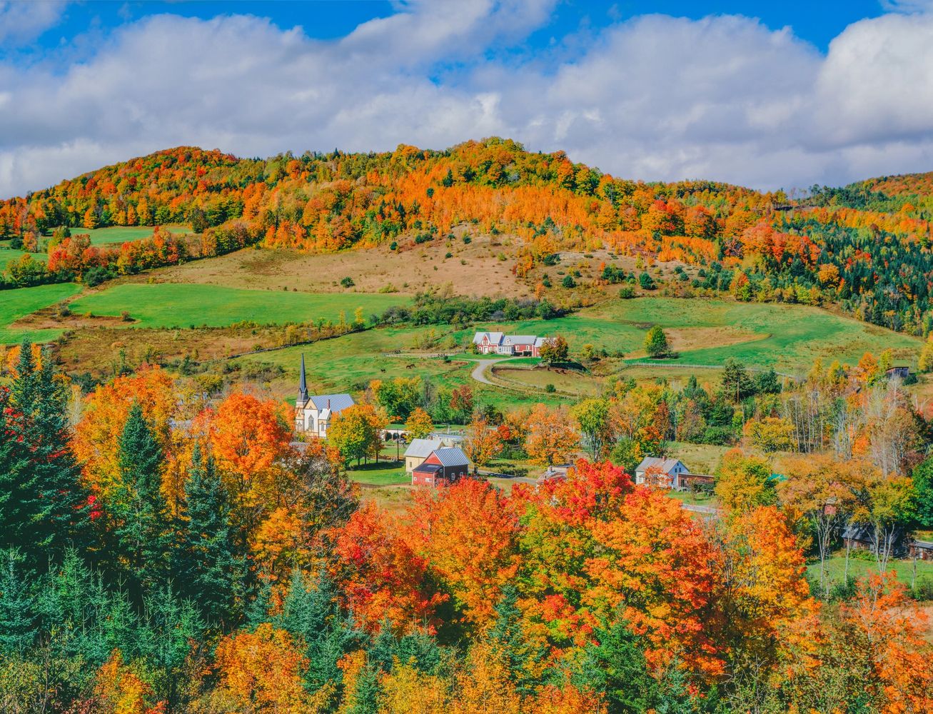 Colorful autumn village nestled in vibrant fall foliage and rolling hills.