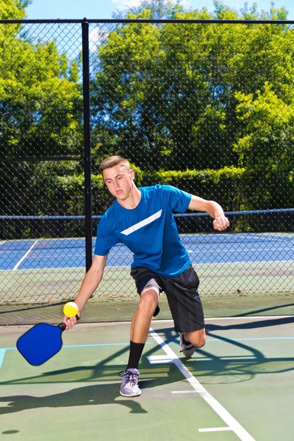 Young man playing pickleball outdoors on a sunny day.