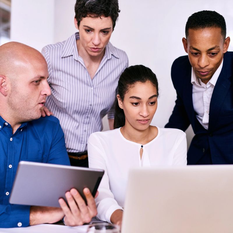 Square image of four multiethnic diverse business people all with their own fresh perspective on the information that everyone is looking at on the laptop computer and electronic tablet.