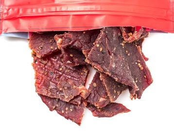 Spicy beef jerky spilling from a partially opened red packet.