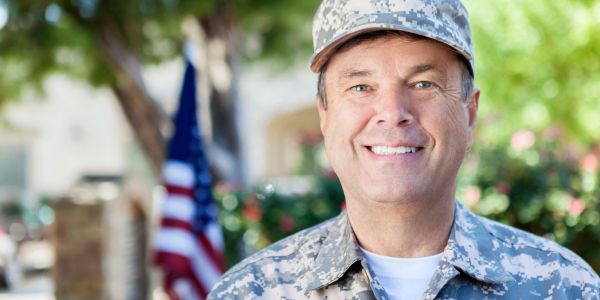 Smiling male soldier outdoors with American flag.
