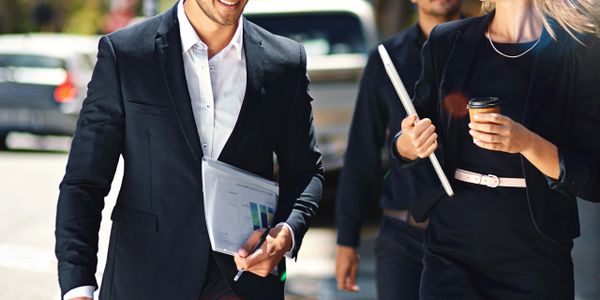 Three professionals walking outdoors, engaged in conversation and holding work documents.