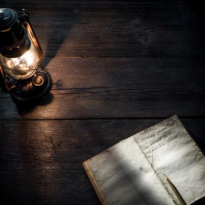 Lantern lighting up an old handwritten book on a wooden table.