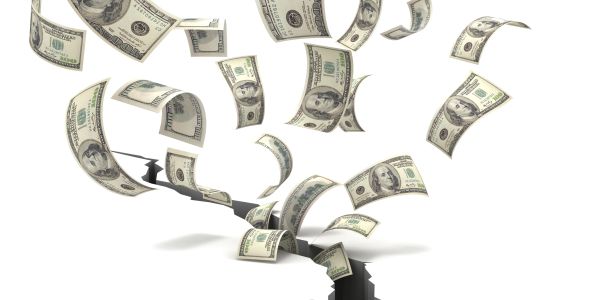 Dollar bills falling into a large crack in the ground.