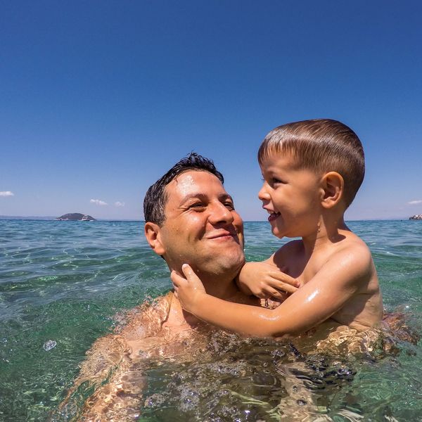 Father and son joyfully swim together in clear ocean water on a sunny day.