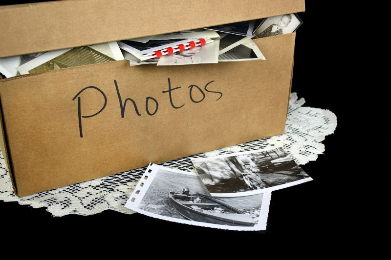Collection of old family photographs in brown cardboard box on lace doily.
