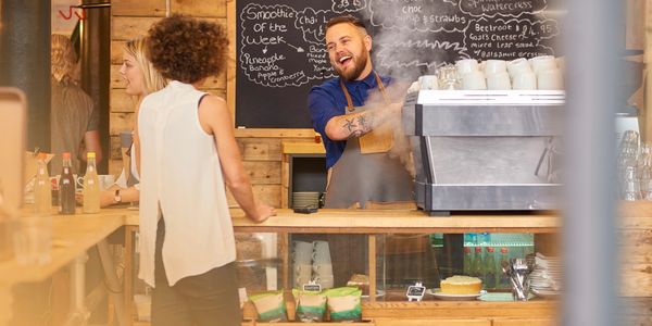 Barista happily serves coffee behind a rustic wooden counter with chalkboard menu.