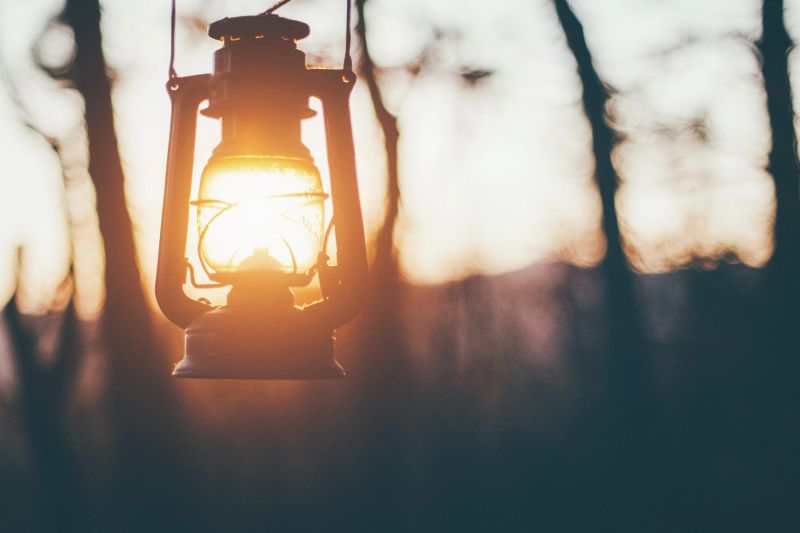 Old lantern hanging in forest, sun shining insted of fire