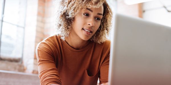 Young woman focused on her laptop in a cozy, sunlit room.
