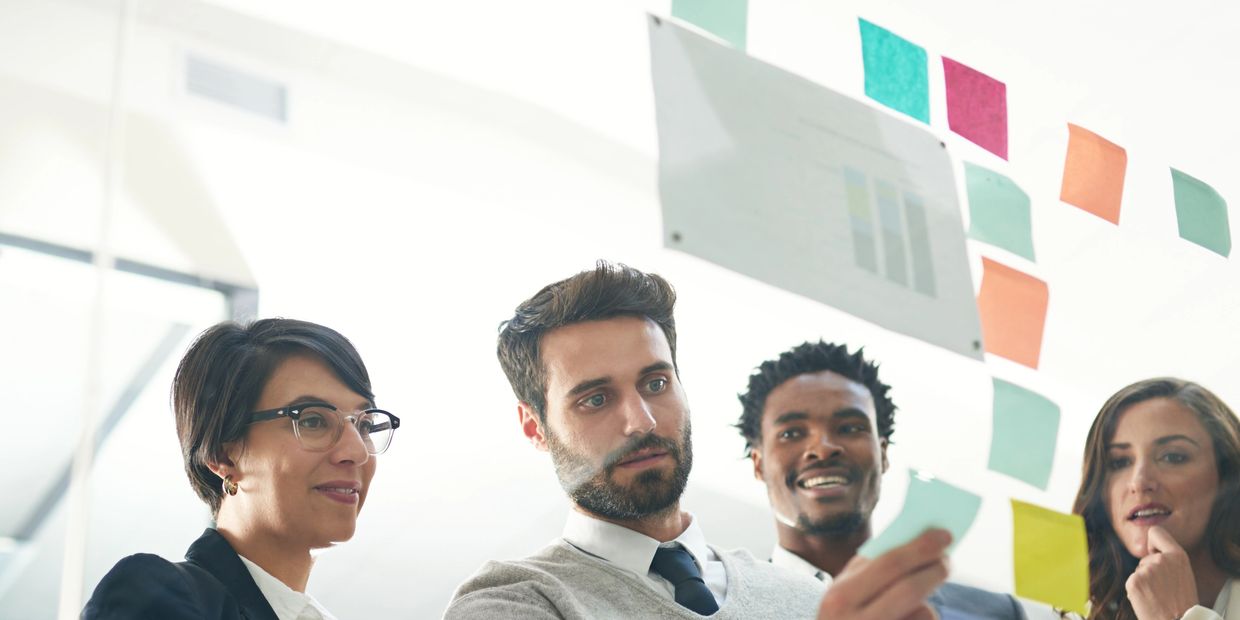 A group of professionals collaborating using sticky notes on a glass wall.