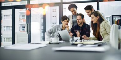 Five colleagues collaborate enthusiastically around a laptop in a modern office.