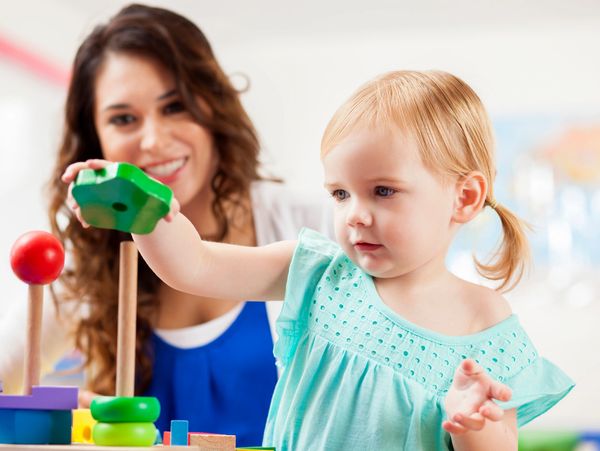 A toddler playing with colorful stacking toys under adult supervision.