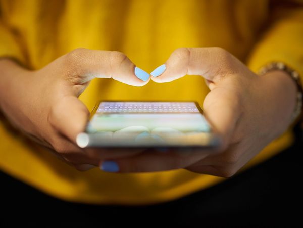 Close-up of hands typing on a smartphone with blue painted nails and a yellow sweater.