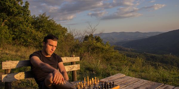 Man sitting alone at a chessboard outdoors during sunset.