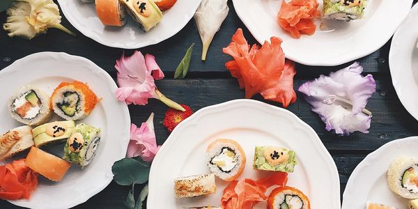 Plates of assorted sushi rolls with pickled ginger and decorative flowers on a dark wooden table.