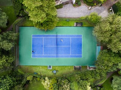 A photo of an empty outdoor tennis court surrounded by lush landscaping in Hillsboro Mile, Fl 