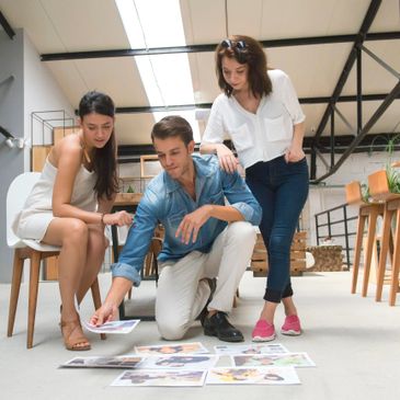 Three colleagues reviewing photos on the floor in a modern office.