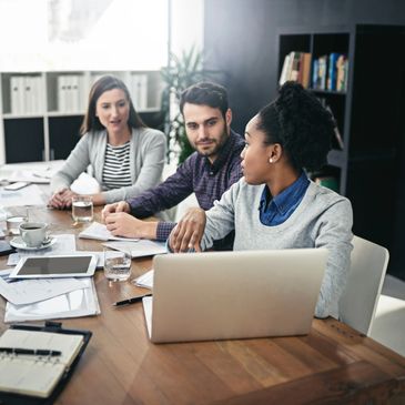 Three colleagues engaged in a discussion around a laptop in a modern office.